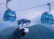 Gloved hand holding up two Bansko lift passes with blue gondola cabins overhead