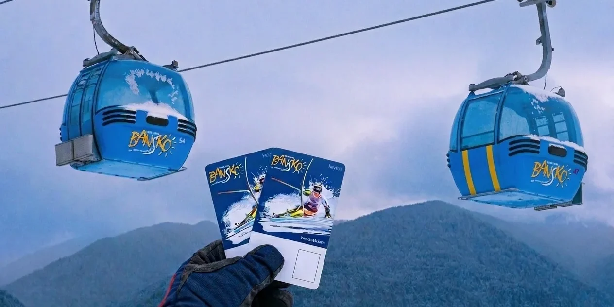 ski-pass-lift Gloved hand holding up two Bansko lift passes with blue gondola cabins overhead